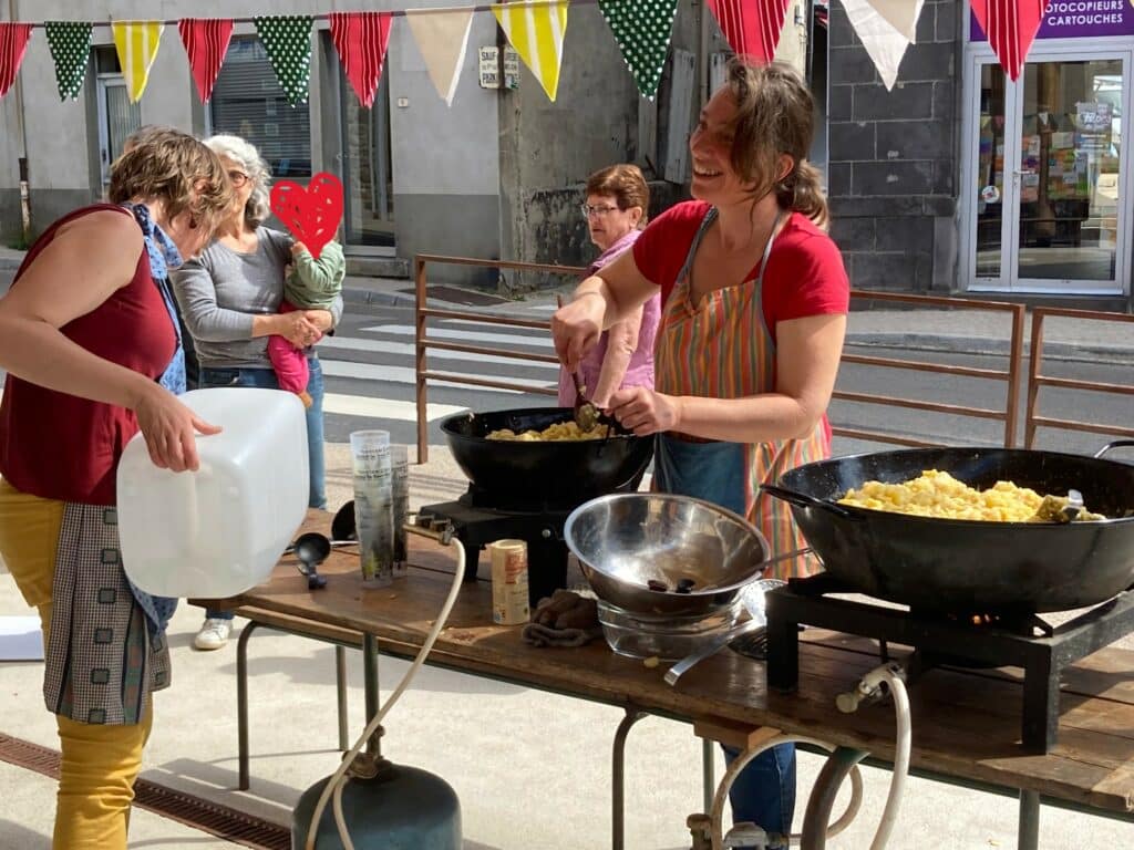 Christine cuisine une truffade au marché de Noirétable, au soleil avec du monde et des fanions